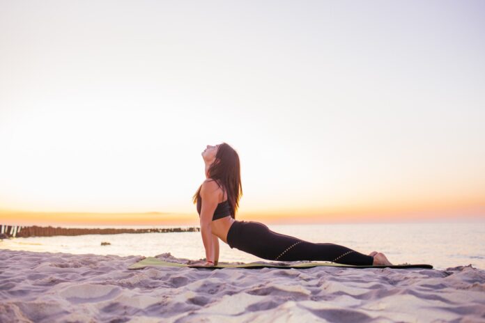 Young slim yogi woman doing Urdhva Mukha Svanasana or Upward Facing Dog Pose against sunset on the beach. Healhy lifestyle concept.